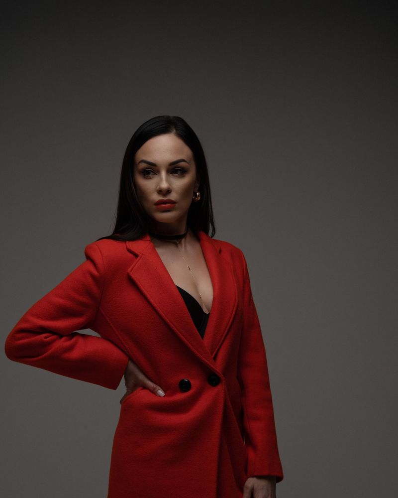 Model in a tailored red wool coat posing against a dark grey studio backdrop
