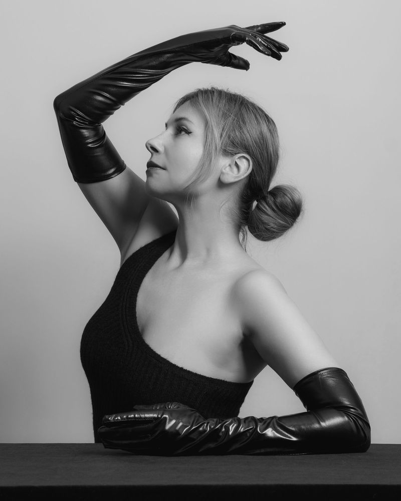 Black-and-white studio portrait of a model in long black leather opera gloves and a one-shoulder top